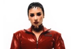 Demi Lovato em Holy Fvck. Artista está de vermelho, com o cabelo curto e olha fixamente para a câmera