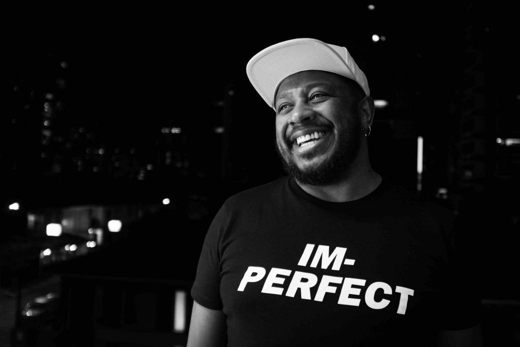 DJ Marky sorrindo, com uma camiseta escrita IM-PERFECT
